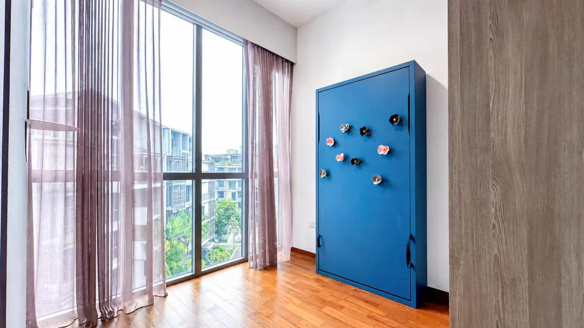 Blue metal cabinet with colorful flower magnets in a sunlit room with large windows and pink sheer curtains on a wooden floor.