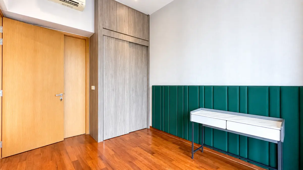 Wooden interior with a large grey built-in closet, light brown doors, and a green upholstered wall panel with a white console table against it.