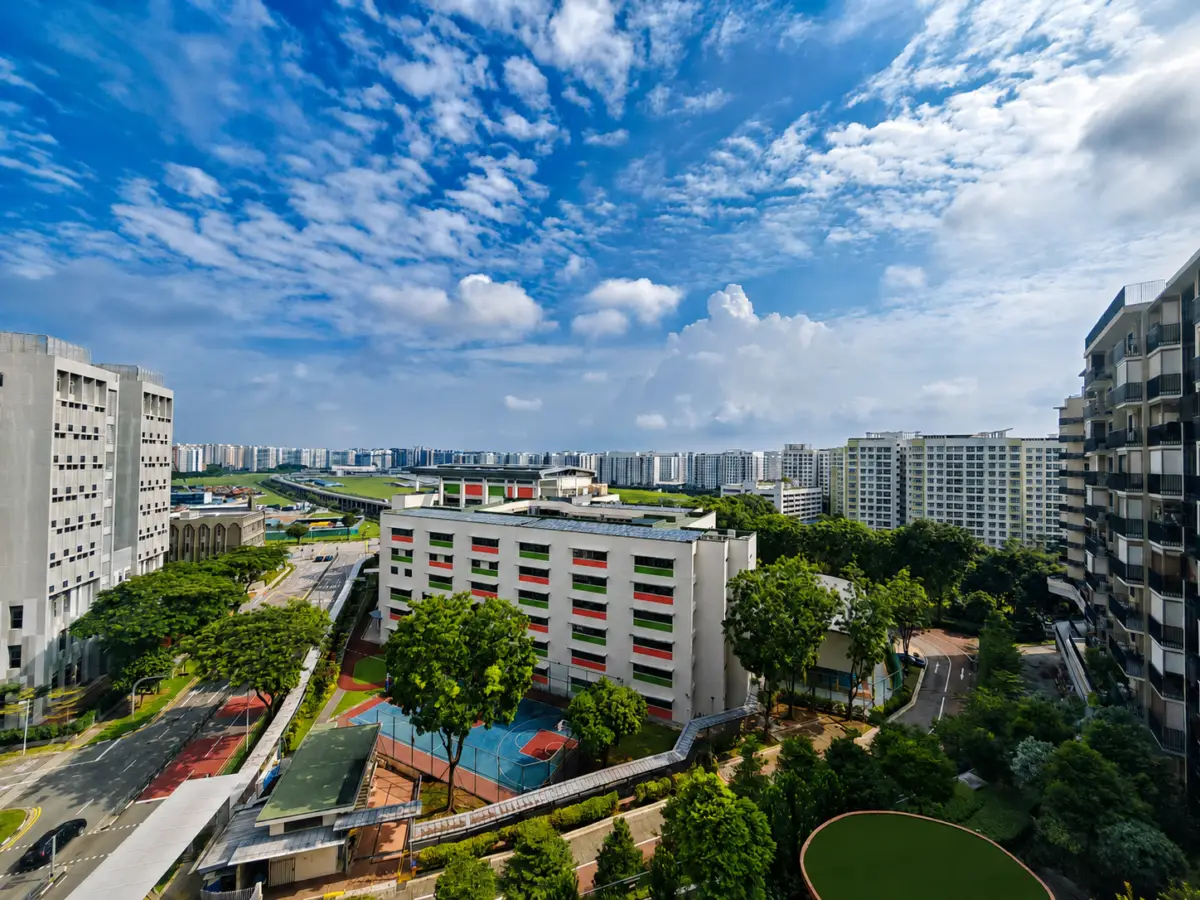 Aerial view of a modern urban campus with white buildings, green trees, and colorful outdoor courts under a bright blue sky with scattered clouds.