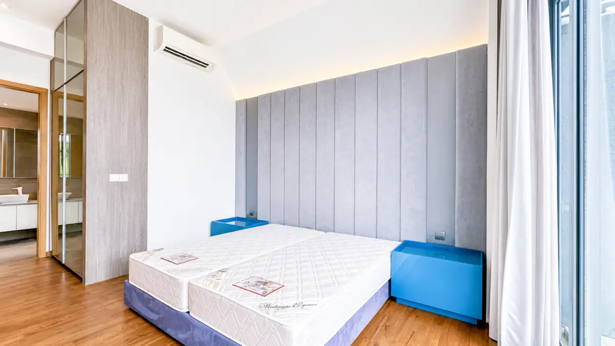 Bright modern hotel room with two twin mattresses on a shared base, a tall gray padded headboard, blue nightstands, wood floors, and large windows with white curtains.