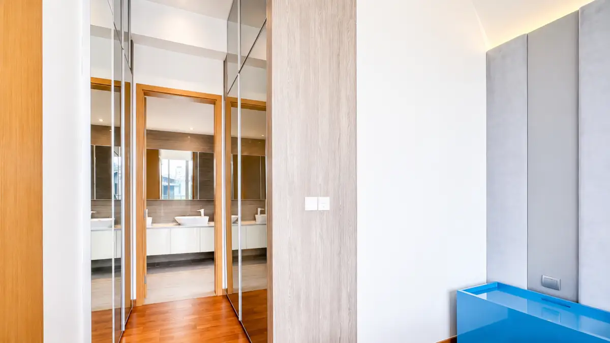 Modern hallway with mirrored panels and warm wood trim leading to a bathroom with two sinks.