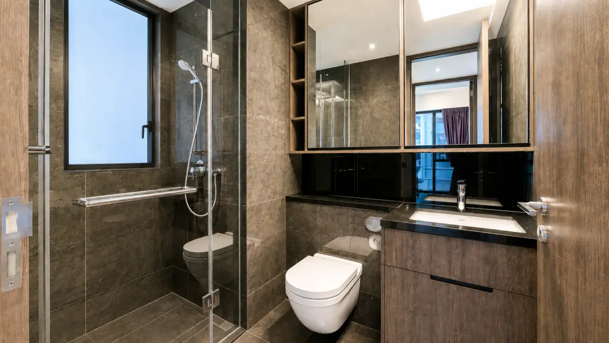Modern bathroom with glass shower enclosure, wall-mounted toilet, and dark wood vanity with a white sink and mirrored cabinets above.
