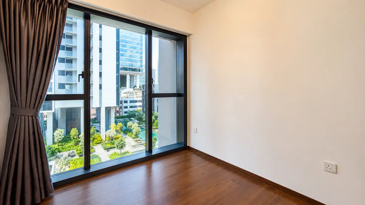 Empty room with dark wood floor and a large window showing a cityscape and greenery outside; brown curtains pulled to the left.