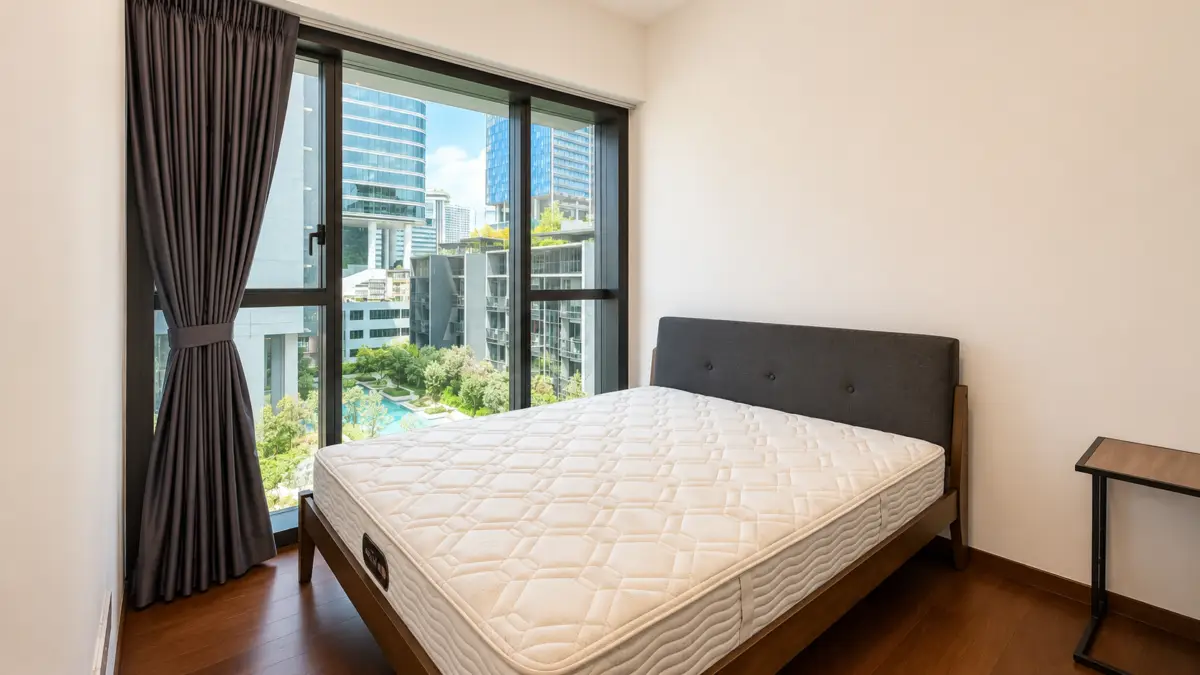 Bedroom with a large window showing city buildings; queen bed with dark upholstered headboard and a small side table nearby.