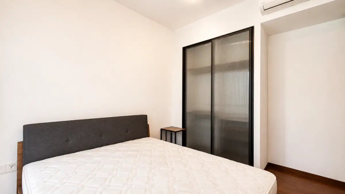 Minimalist bedroom with a double bed, grey headboard, small nightstand, and frosted glass sliding doors.